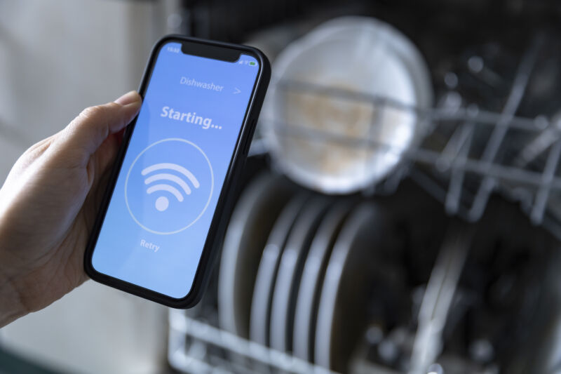 Woman with smartphone operating smart dishwasher